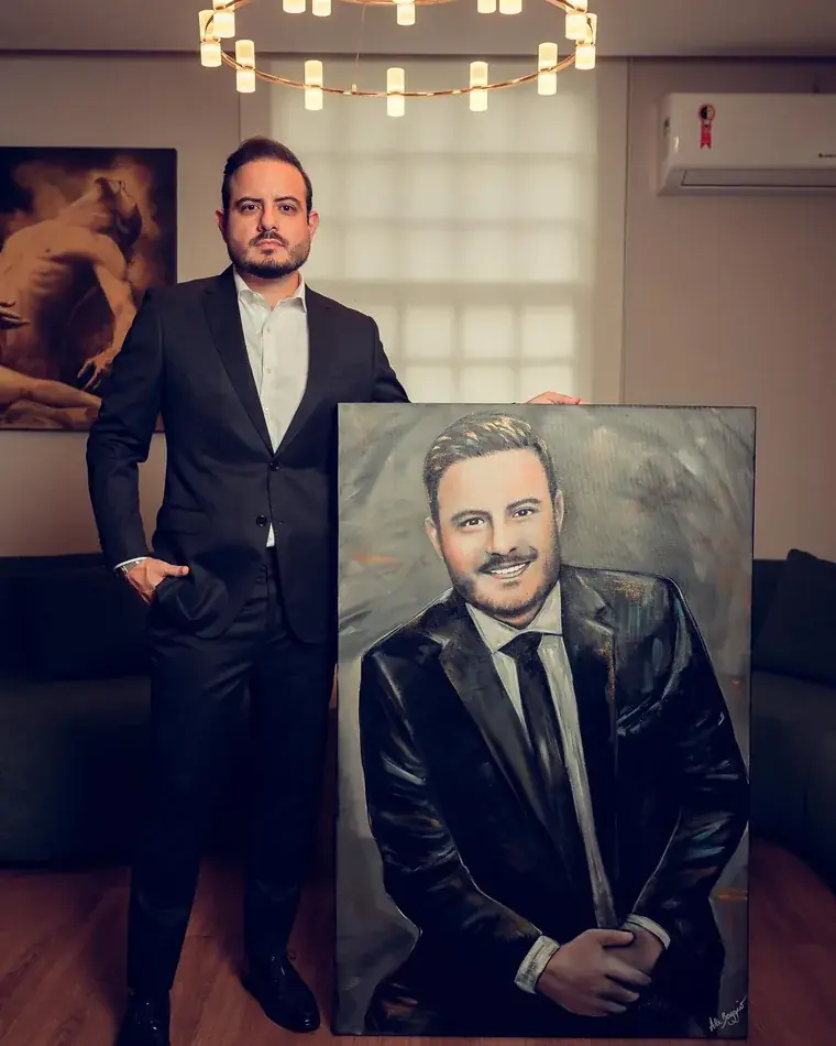 Cliente de terno ao lado do retrato dele pintado por Ale Baggio